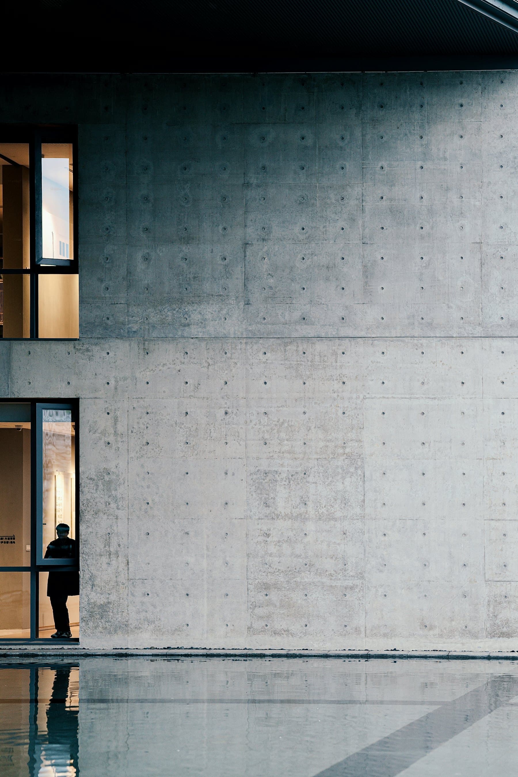 A board-formed concrete wall meeting a still reflecting pool